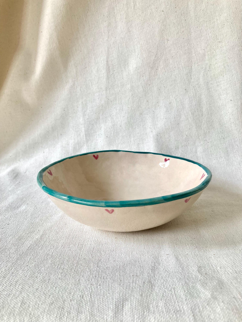 Peut inclure: Un bol en céramique fait à la main avec un intérieur crème et un bord turquoise. De petits cœurs roses sont peints autour du bord. Un objet de cuisine unique.