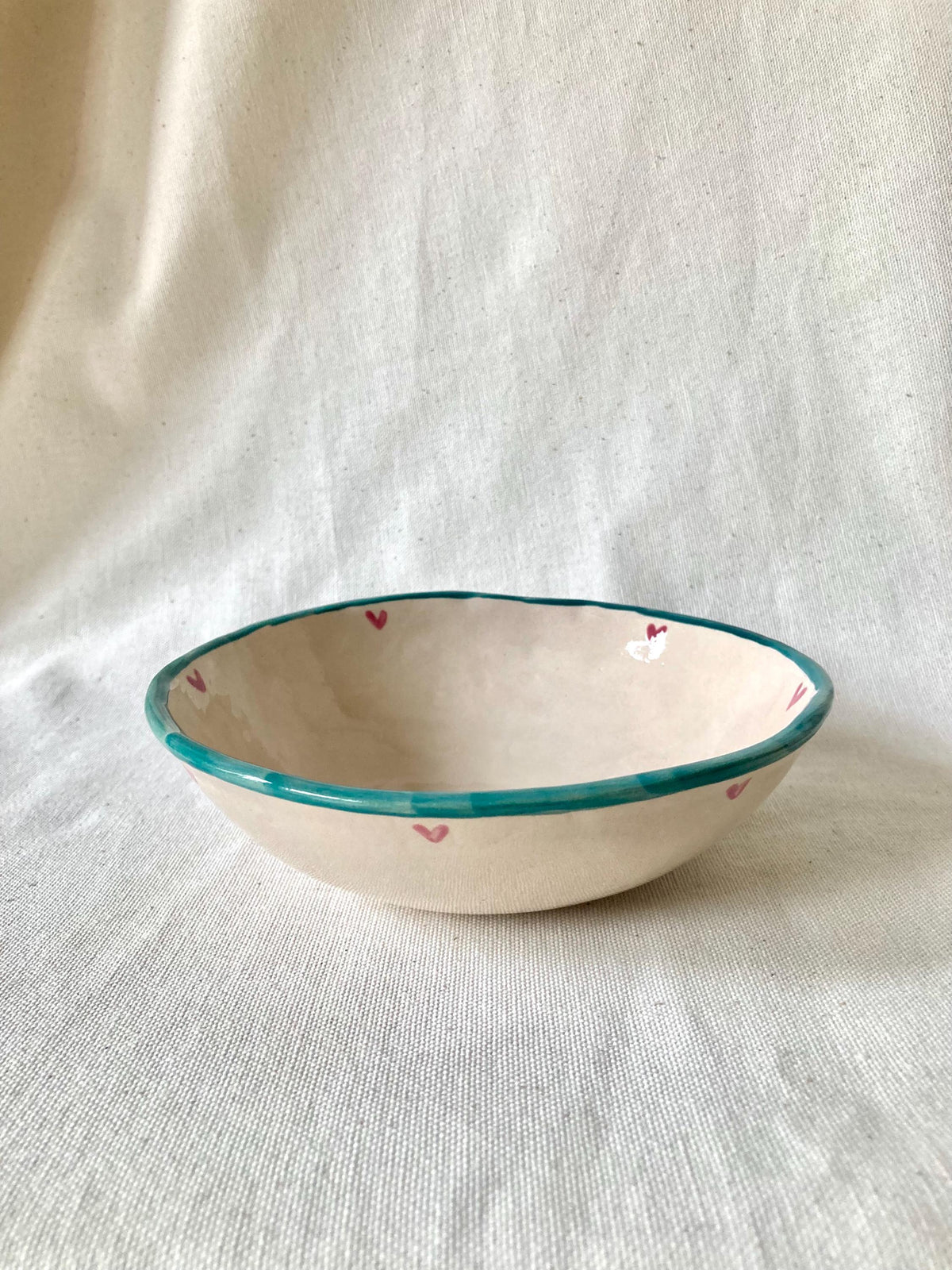 Peut inclure: Un bol en céramique fait à la main avec un intérieur crème et un bord turquoise. De petits cœurs roses sont peints autour du bord. Un objet de cuisine unique.