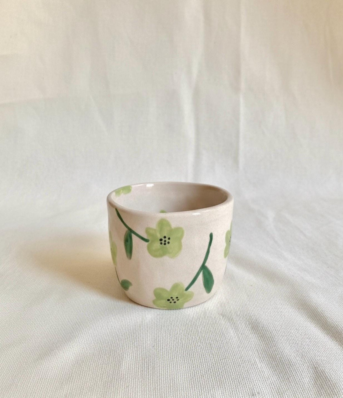 Peut inclure: Une petite tasse en céramique blanc cassé avec un motif floral peint à la main. Les fleurs sont vert clair avec des tiges et des feuilles vert foncé. La tasse est cylindrique et semble faite à la main.