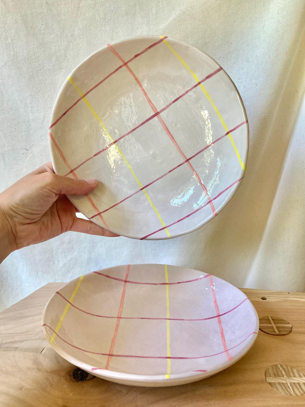 Peut inclure: Deux assiettes en céramique, une ronde et une ovale, avec un fond gris clair et un motif à carreaux de lignes jaunes, rouges et roses. L'assiette ronde est tenue par une main.